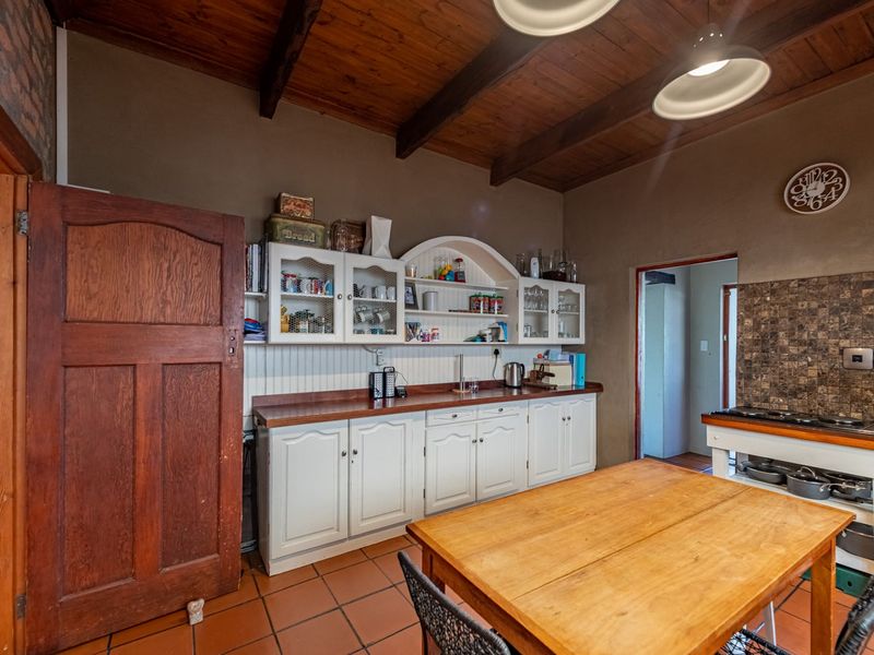 A rustic kitchen featuring timber ceilings with exposed beams, tiled flooring, built-in cabinetry, and a stone tile backsplash with an integrated hob.
