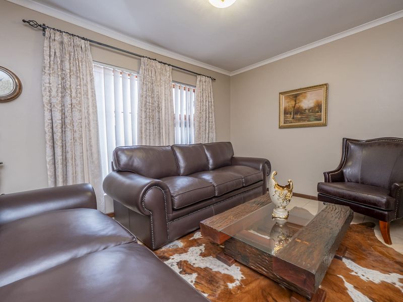 A comfortable living room featuring tiled flooring and large windows with vertical blinds, providing a neutral space for relaxation.