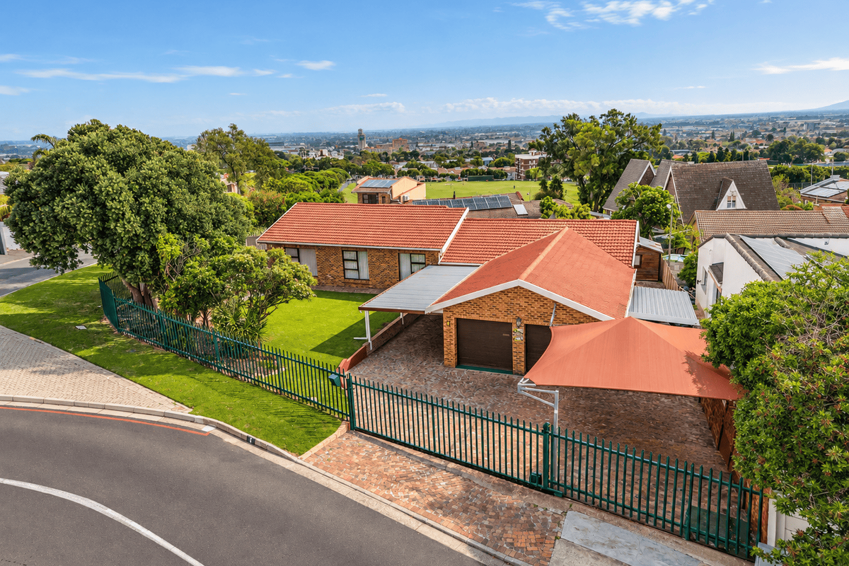 Aerial view of a well-maintained brick house featuring a terracotta roof, double garage, paved driveway, and secure perimeter fencing in a suburban setting.