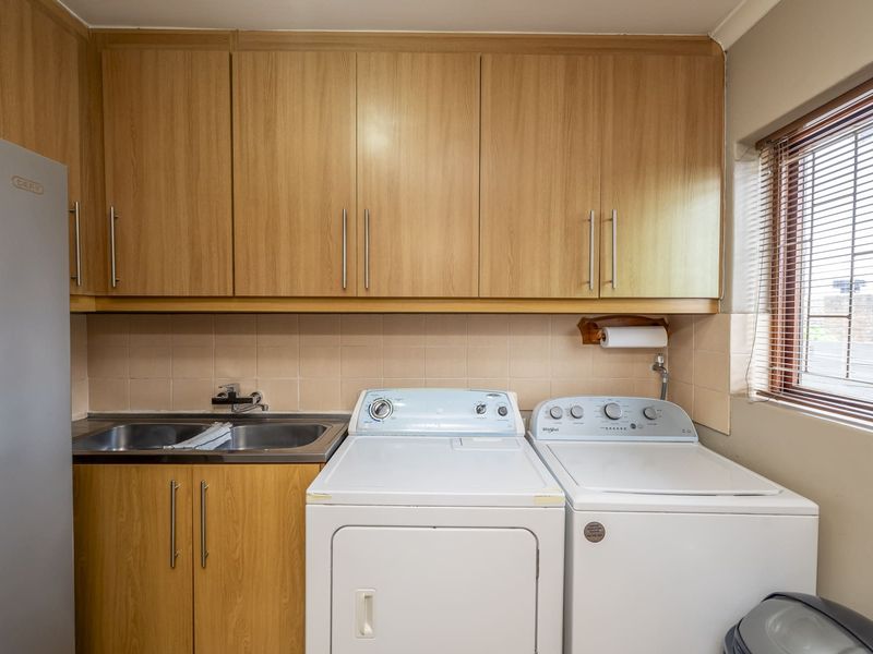 A functional laundry room featuring built-in wood-finish cabinetry, a stainless steel sink, and dedicated space for laundry appliances.