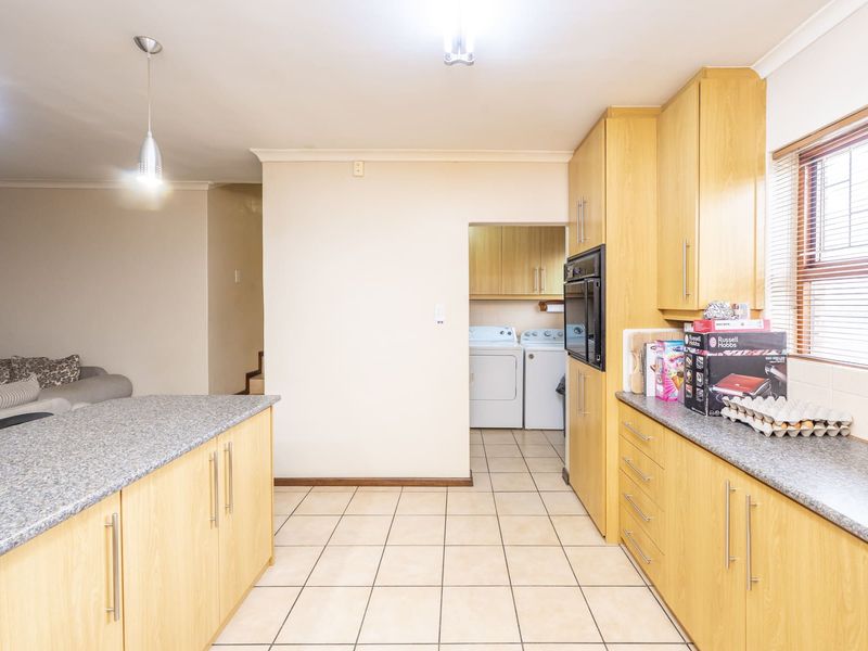 A functional kitchen featuring light wood cabinetry, granite countertops, and tiled flooring, with an adjacent scullery area visible in the background.
