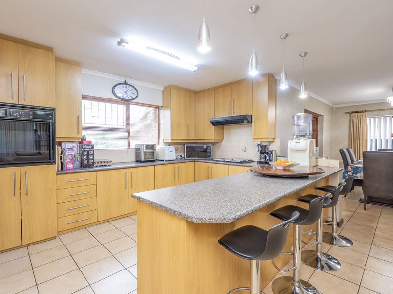 Spacious open-plan kitchen featuring light wood cabinetry, granite countertops, a central island with breakfast bar seating, and tiled flooring throughout.