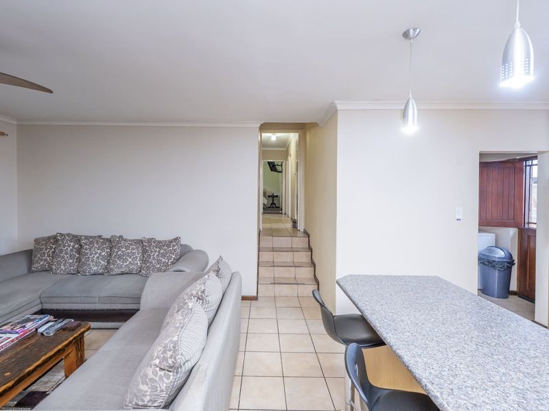 Open-plan living area featuring tiled flooring, a granite breakfast bar, and a built-in oven, with a step-up transition to the hallway.