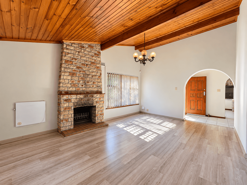 Spacious living room featuring a prominent stone fireplace, vaulted timber beam ceiling, and light-toned laminate flooring, leading to an arched entryway.