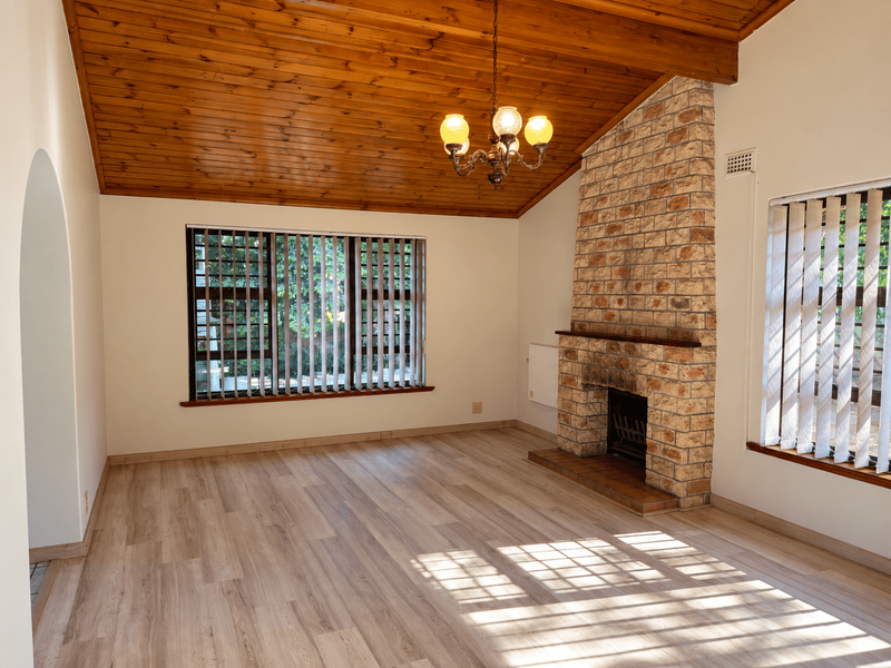 Spacious living room featuring a prominent stone fireplace, vaulted timber-clad ceiling, and modern laminate flooring, offering a bright and inviting atmosphere.