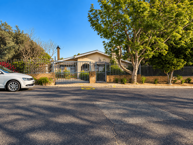 Front elevation of a residential property featuring a brick boundary wall, metal security fencing, and gated access from the street.