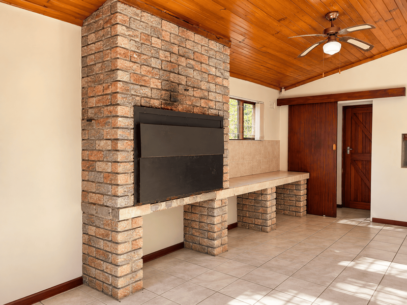 Covered patio area featuring a built-in brick braai, tiled flooring, and a timber ceiling with a fitted ceiling fan.
