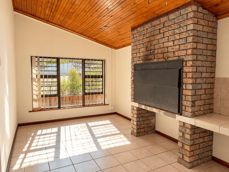 Spacious living area featuring a prominent exposed brick fireplace, warm timber ceiling, and tiled flooring, offering a versatile space for relaxation.
