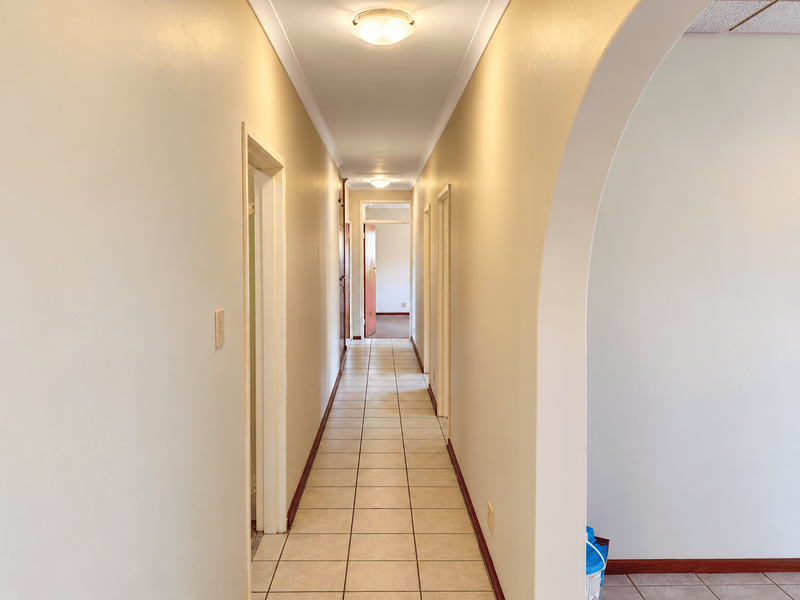 A clean, well-lit hallway featuring neutral walls, tiled flooring, and an architectural archway leading to the interior living spaces.