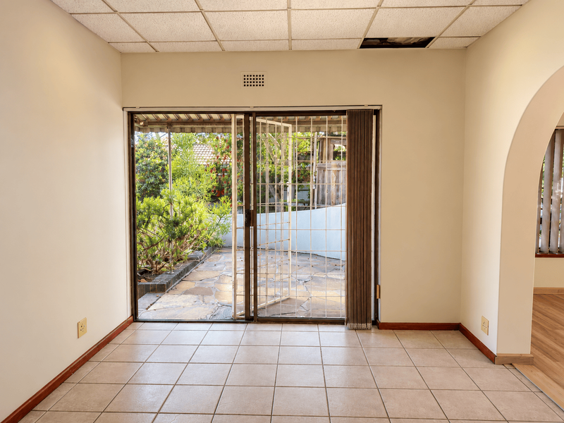An empty living room featuring tiled flooring, a drop ceiling with a missing panel, and a sliding glass door leading to an outdoor patio area.