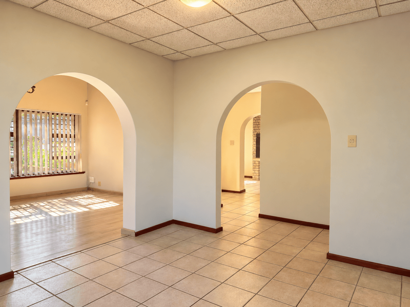 Spacious living area featuring distinctive arched doorways, ceramic tile flooring, and a drop ceiling, offering a bright and open layout.