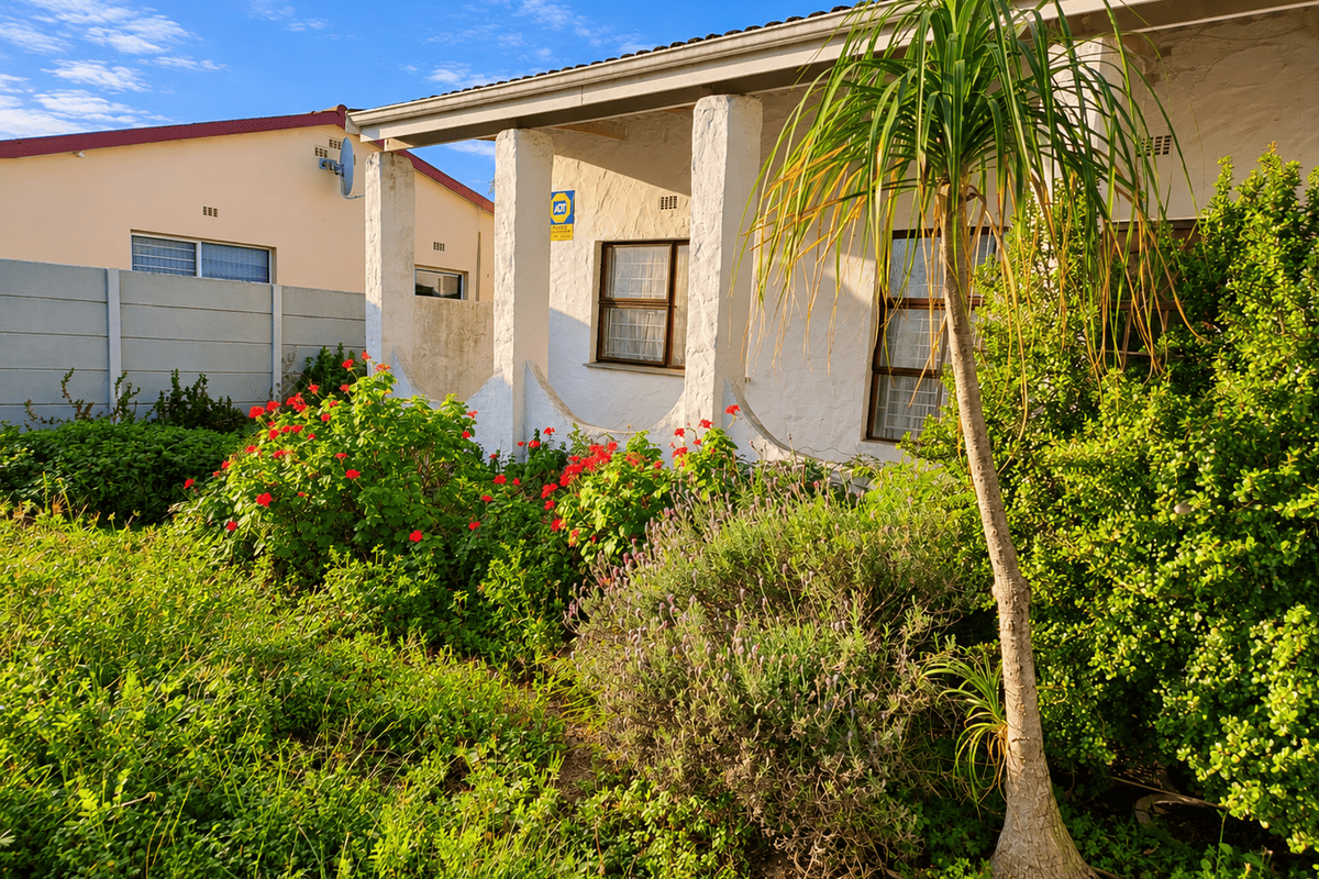Front elevation of the house featuring a covered patio area with concrete pillars, established garden landscaping, and a security alarm system.