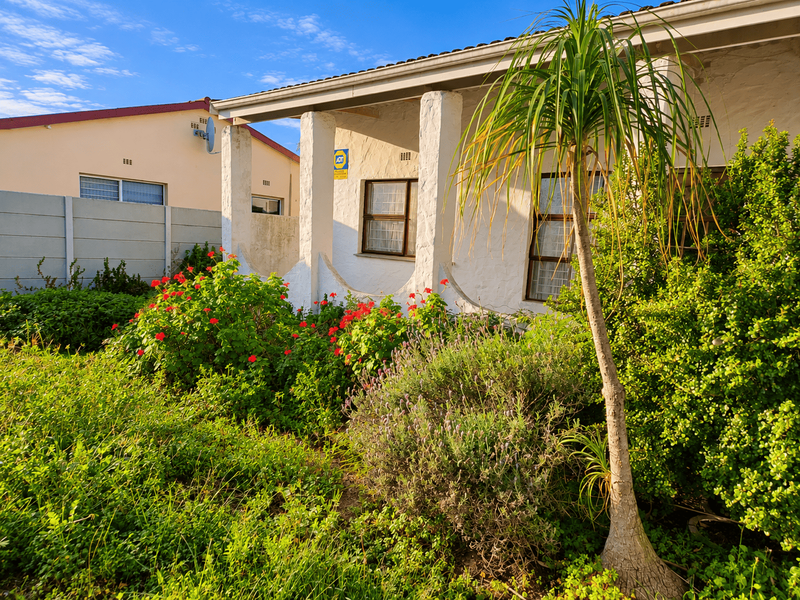 Front elevation of the house featuring a covered patio area with concrete pillars, established garden landscaping, and a security alarm system.