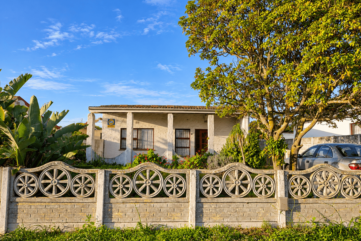 Front view of a single-story house featuring a decorative concrete fence, covered porch, and established garden setting.
