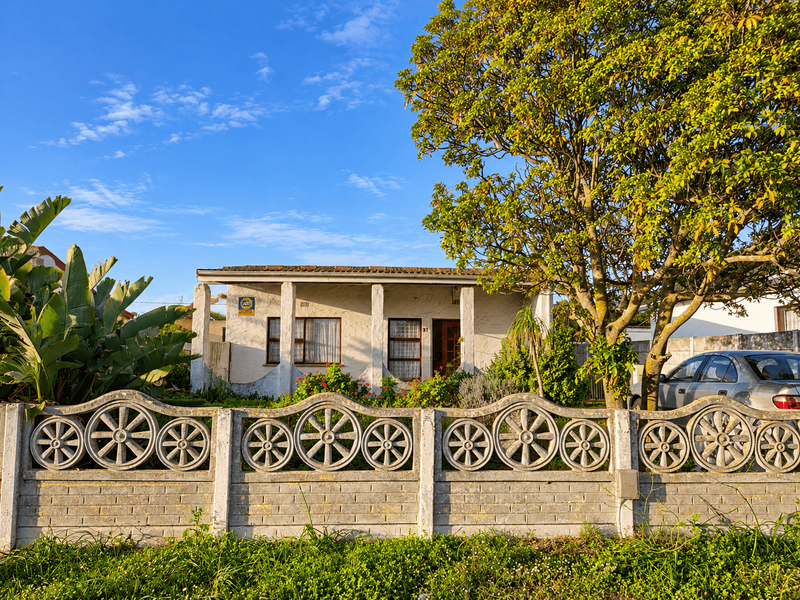 Front view of a single-story house featuring a decorative concrete fence, covered porch, and established garden setting.