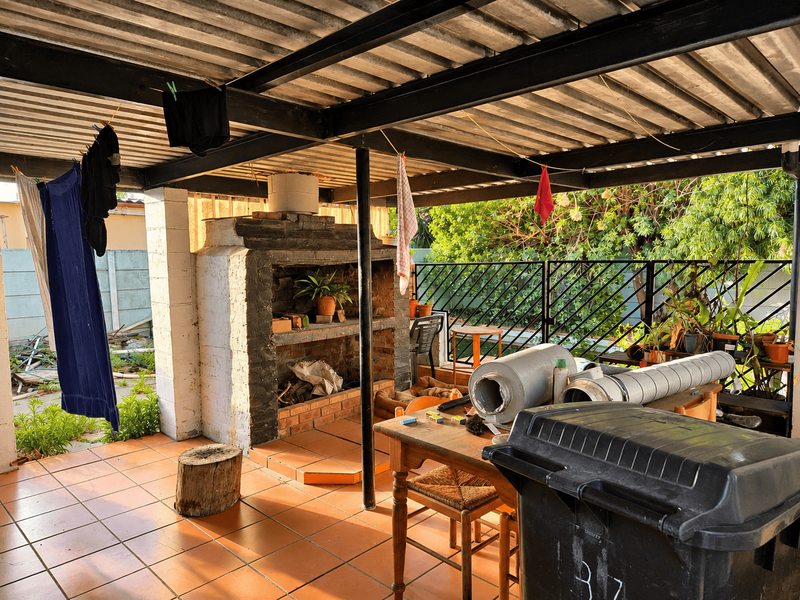 Covered outdoor patio area featuring a built-in brick braai, tiled flooring, and a corrugated metal roof structure.