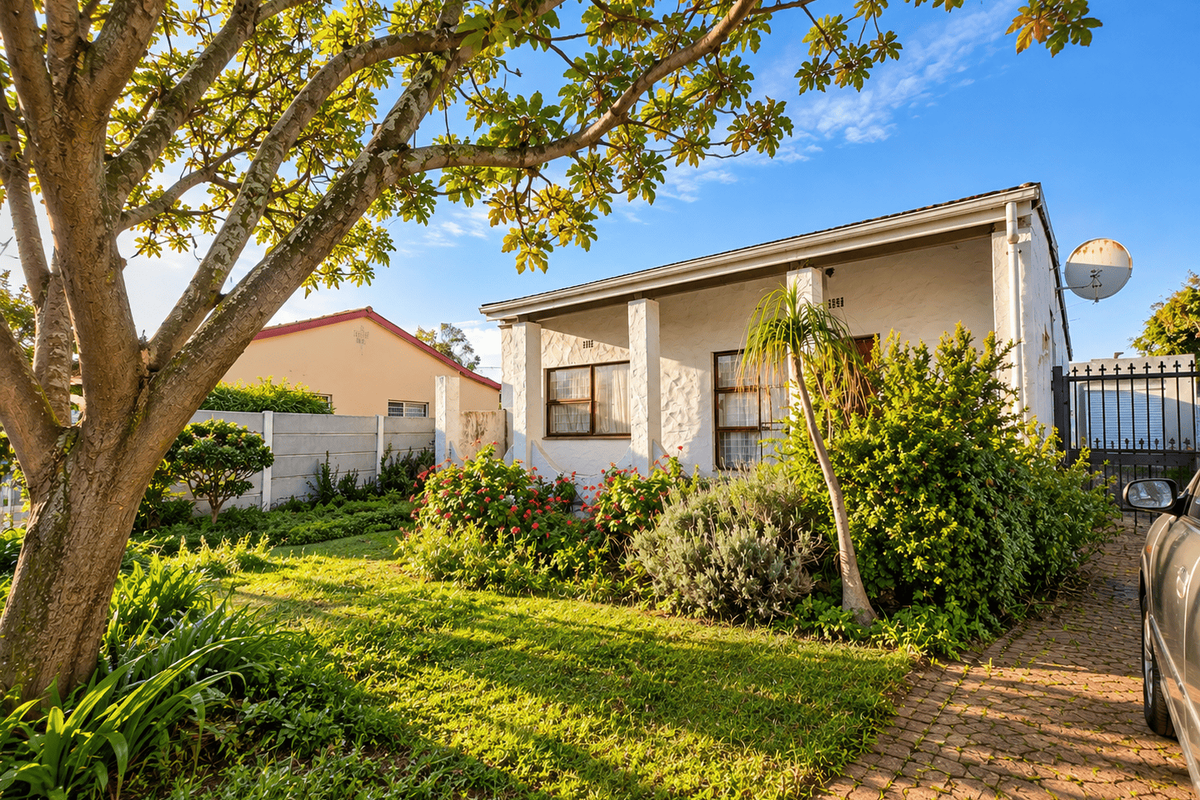 Front view of a single-story house featuring a paved driveway, established garden, and secure gated entrance.
