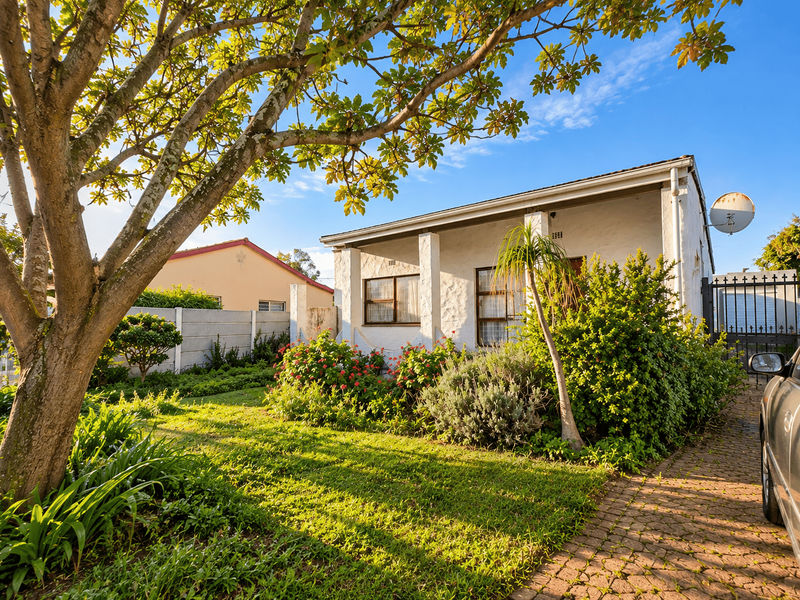Front view of a single-story house featuring a paved driveway, established garden, and secure gated entrance.