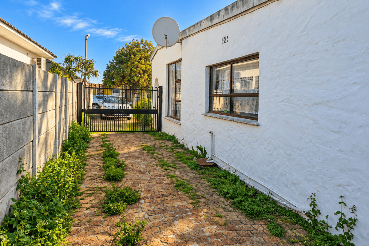 Side view of the property featuring a paved driveway, metal security gate, and precast concrete boundary wall with exterior wall access.
