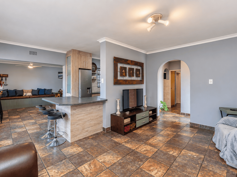 Open plan living area featuring a central kitchen island, tiled flooring, and a distinctive arched entryway leading to the hallway.