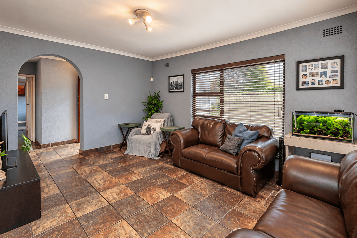 A comfortable living room featuring tiled flooring, an arched entryway, and large windows fitted with venetian blinds.