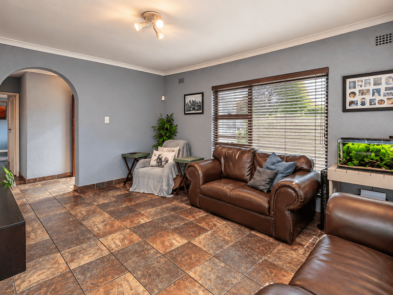 A comfortable living room featuring tiled flooring, an arched entryway, and large windows fitted with venetian blinds.