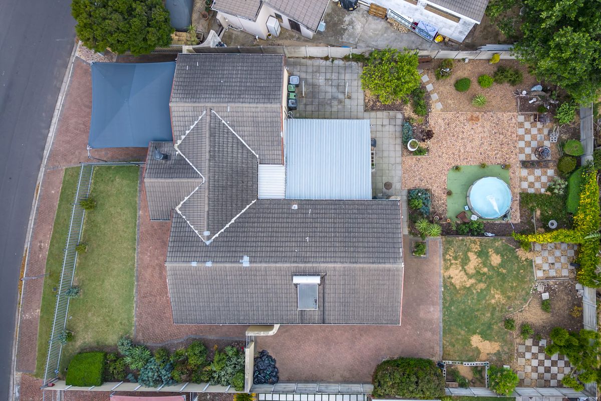 Aerial view of the property showing the roof structure, paved driveway, swimming pool, garden areas, and covered patio space.