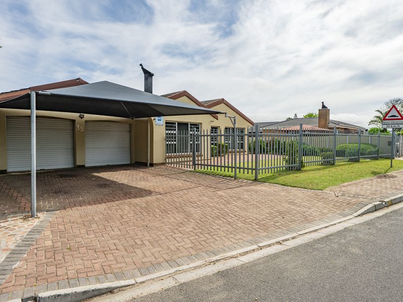 Front exterior view of the property featuring a paved driveway, double garage with roller shutter doors, shade sail carport, and secure steel perimeter fencing.