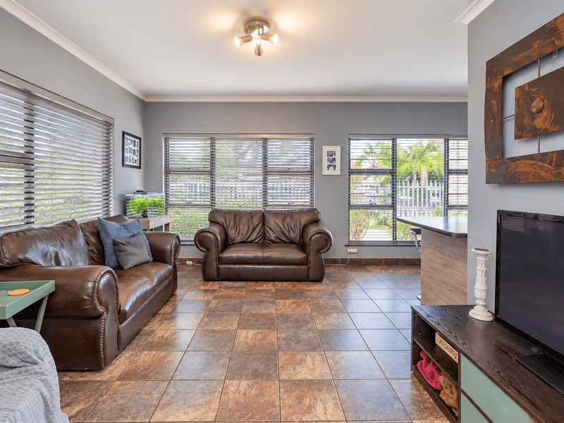 Spacious living area featuring durable tiled flooring, large windows with venetian blinds, and a convenient breakfast bar counter.
