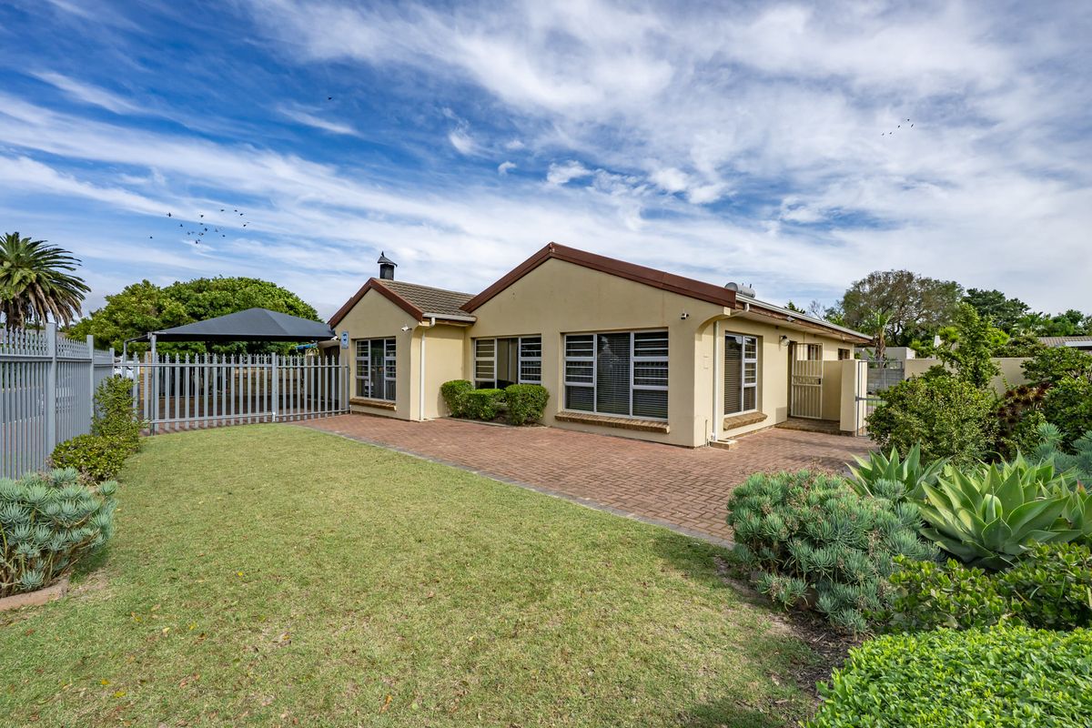 Rear view of the property featuring a paved patio area, well-maintained lawn, perimeter fencing, and established garden landscaping.