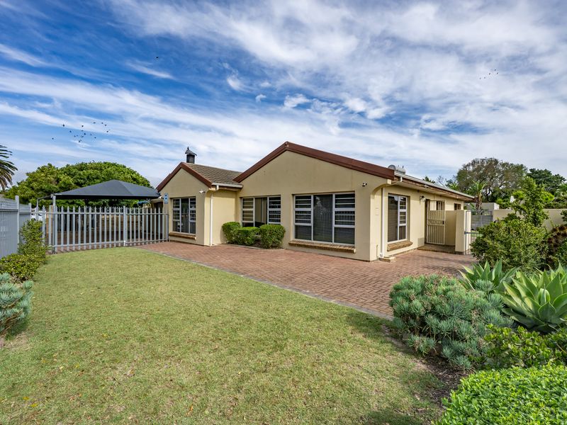 Rear view of the property featuring a paved patio area, well-maintained lawn, perimeter fencing, and established garden landscaping.