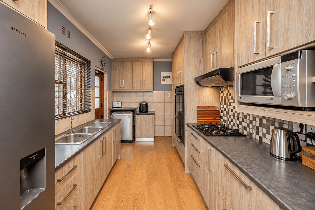 A functional galley-style kitchen featuring wood-look cabinetry, dark laminate countertops, a gas hob, built-in oven, and a tiled backsplash.