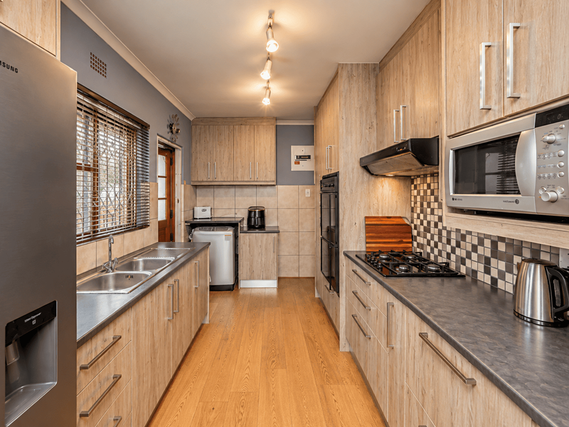 A functional galley-style kitchen featuring wood-look cabinetry, dark laminate countertops, a gas hob, built-in oven, and a tiled backsplash.