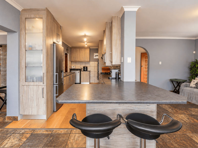 Open-plan kitchen featuring modern laminate cabinetry, a breakfast bar, and tiled flooring, seamlessly connecting to the adjacent living area.