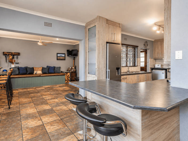 Open-plan kitchen and living area featuring modern wood-look cabinetry, a breakfast bar, tiled flooring, and a built-in bench seating area.