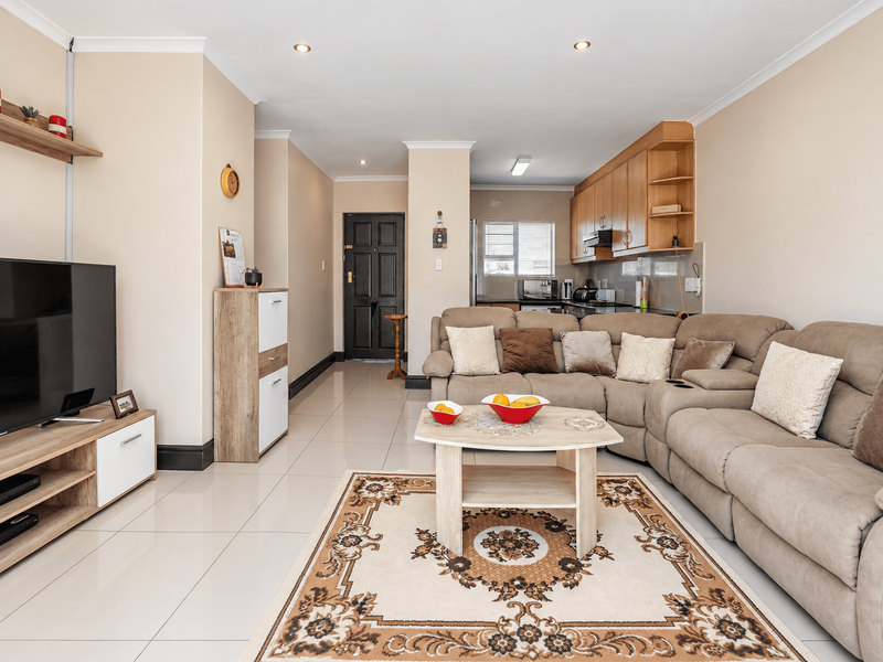 An open-plan living and kitchen area featuring tiled flooring, recessed lighting, and functional built-in cabinetry, creating a cohesive and practical living space.