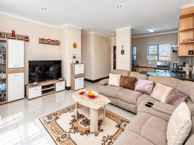 An open-plan living area featuring tiled floors, recessed lighting, and a modern kitchen with built-in cabinetry and appliances.