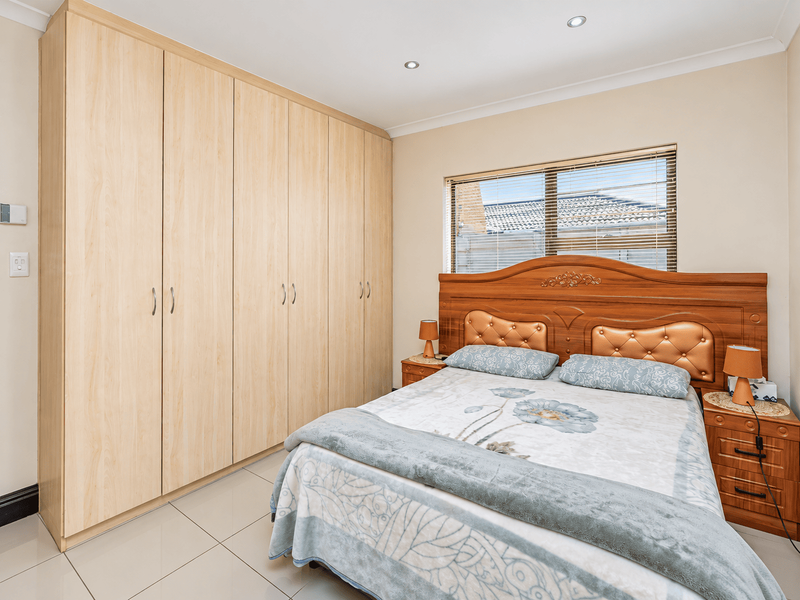 A well-maintained bedroom featuring light wood-toned built-in wardrobes, tiled flooring, and recessed ceiling lighting, providing a clean and functional living space.