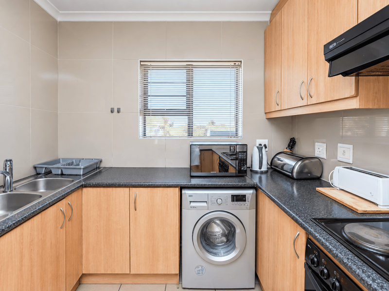 Functional kitchen featuring light wood cabinetry, granite countertops, integrated washing machine, and built-in cooking appliances with a tiled splashback.