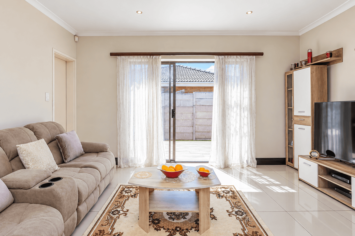 A bright and well-maintained living room featuring tiled flooring, recessed downlights, and a sliding glass door providing access to the rear patio.