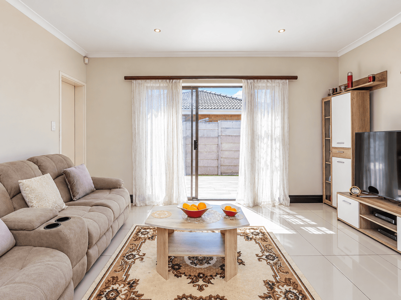 A bright and well-maintained living room featuring tiled flooring, recessed downlights, and a sliding glass door providing access to the rear patio.