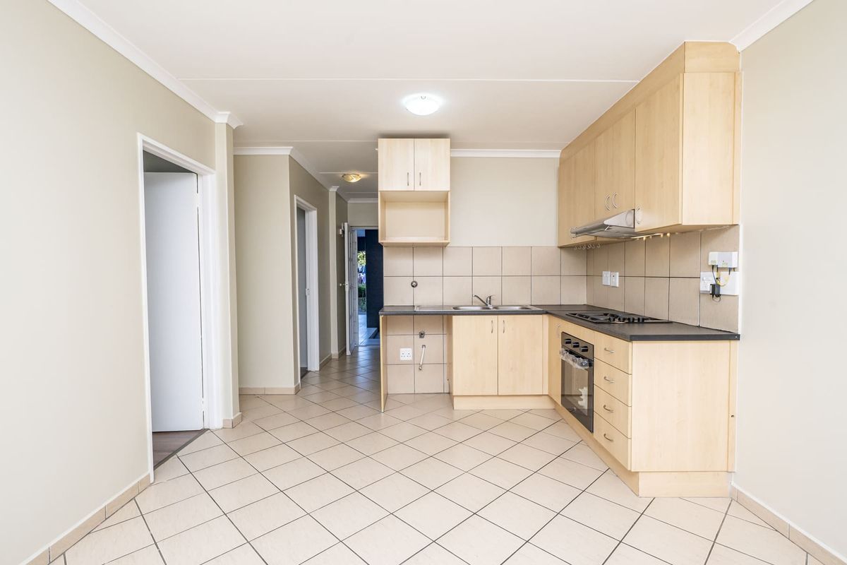 A functional kitchen featuring light wood cabinetry, laminate countertops, a built-in oven with gas hob, and tiled flooring throughout.