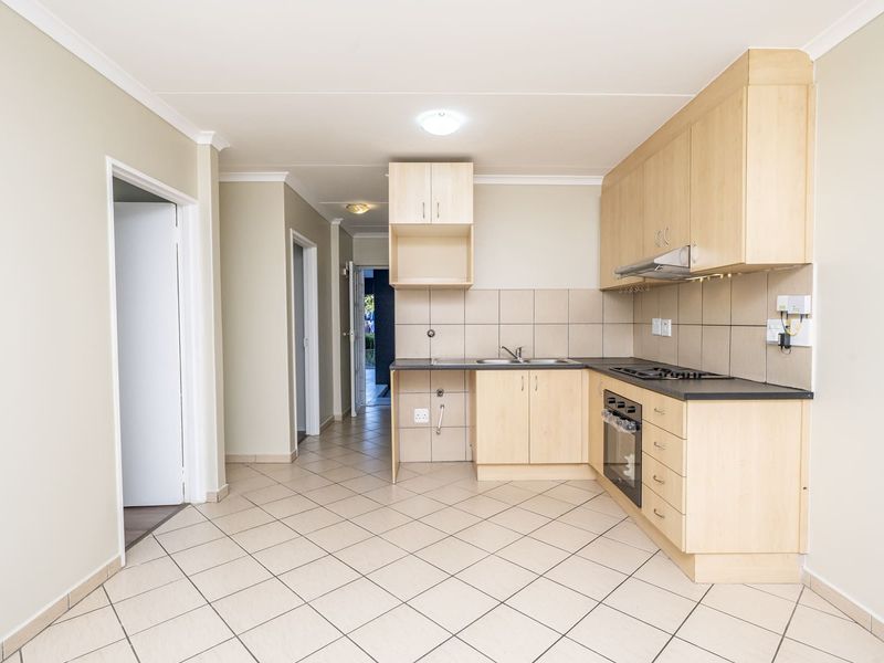A functional kitchen featuring light wood cabinetry, laminate countertops, a built-in oven with gas hob, and tiled flooring throughout.