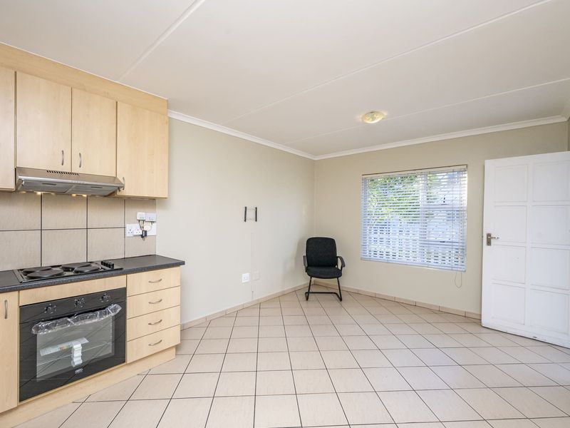 Open-plan kitchen and living area featuring light wood cabinetry, built-in oven and hob, tiled flooring, and neutral wall finishes.