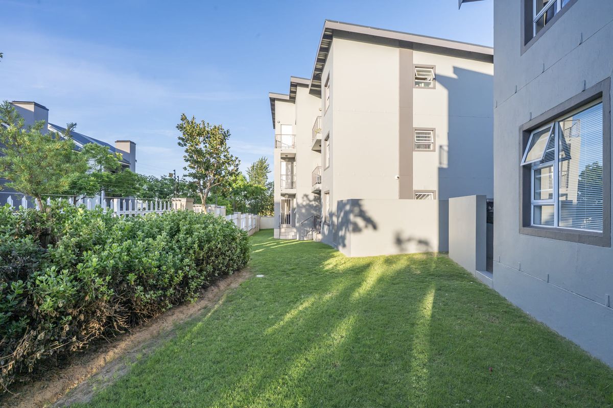 A well-maintained rear exterior view of a modern apartment complex featuring a manicured lawn, landscaped garden borders, and contemporary building facade.
