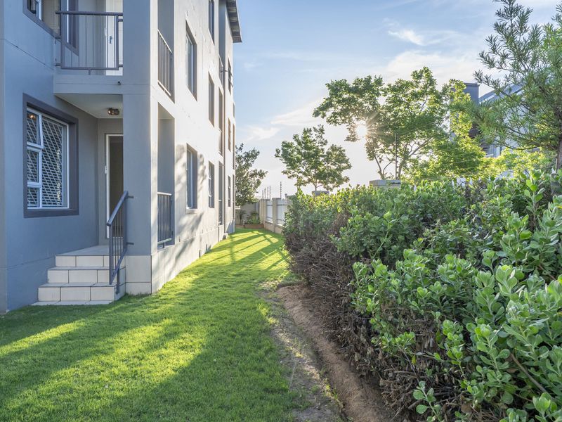 A well-maintained rear exterior view of the apartment building featuring a manicured lawn, landscaped hedge, and secure access steps.