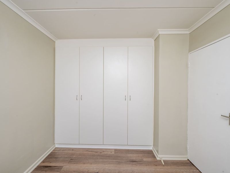 A clean, empty bedroom featuring neutral walls, modern laminate flooring, and ample built-in cupboard storage space.