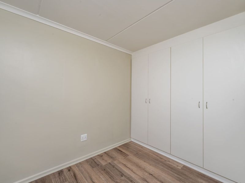 A clean, empty bedroom featuring neutral walls, modern laminate flooring, and ample built-in cupboard storage.