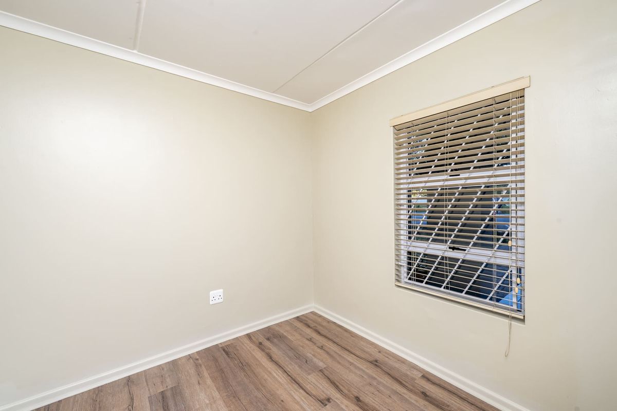 A clean, empty bedroom featuring modern laminate flooring, neutral wall paint, and fitted venetian blinds, offering a versatile space ready for personalization.
