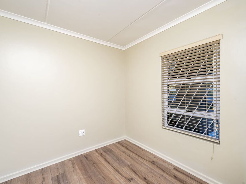 A clean, empty bedroom featuring modern laminate flooring, neutral wall paint, and fitted venetian blinds, offering a versatile space ready for personalization.